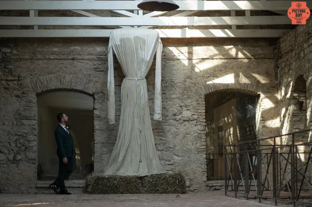 groom looks at suspended wedding dress rustic venue — GOGA Photography
